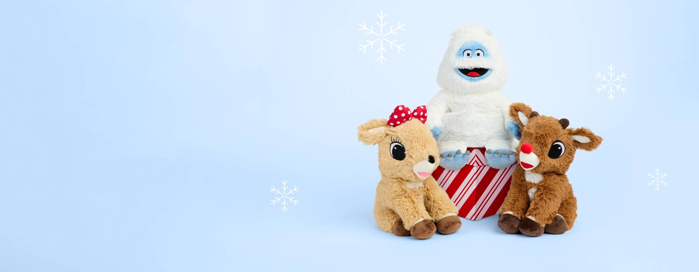 Clarice Warmies, Bumble Warmies and Rudolph Warmies sitting around a present wrapped in red and white paper