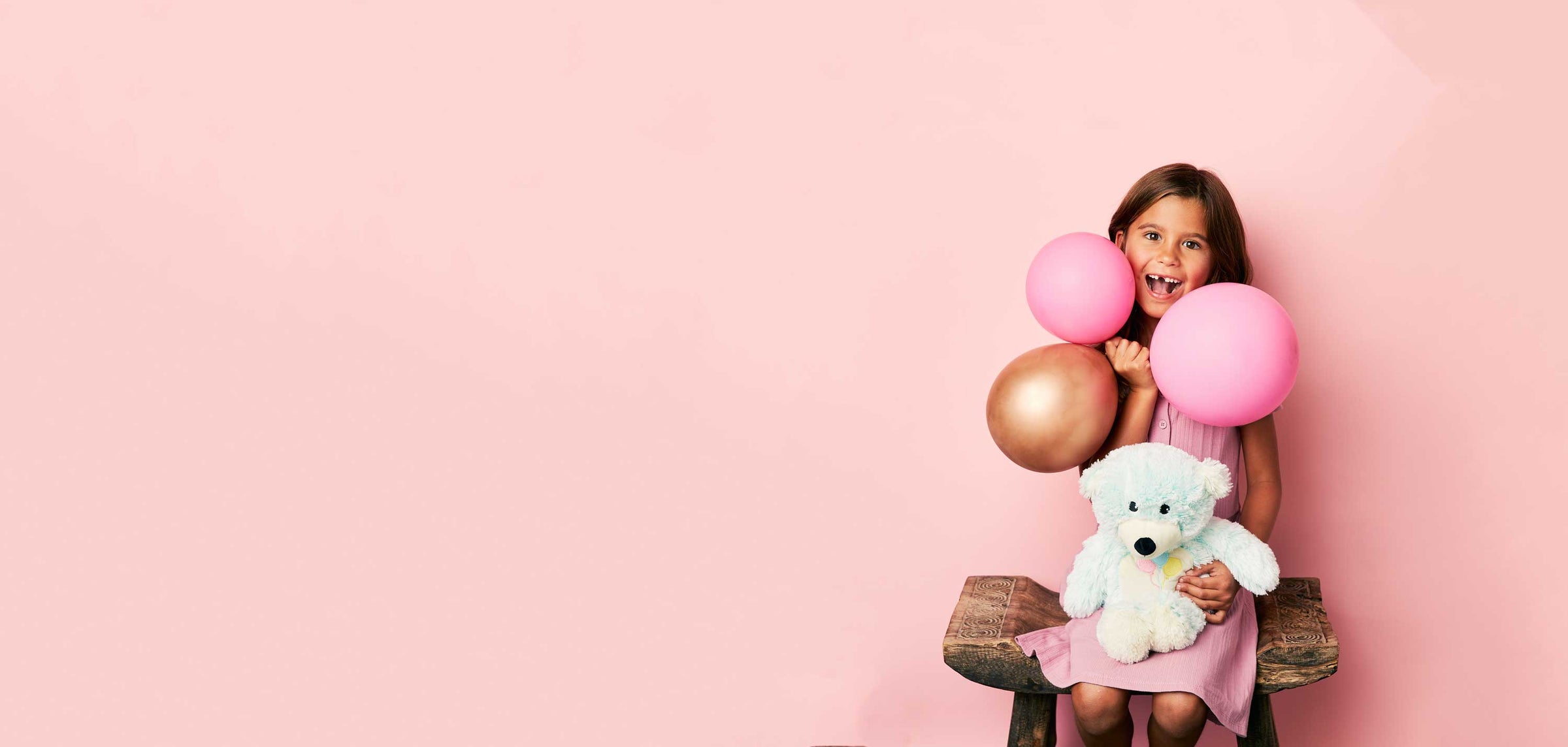 Child smiling holding balloons while holding a Celebration Bear Warmies.